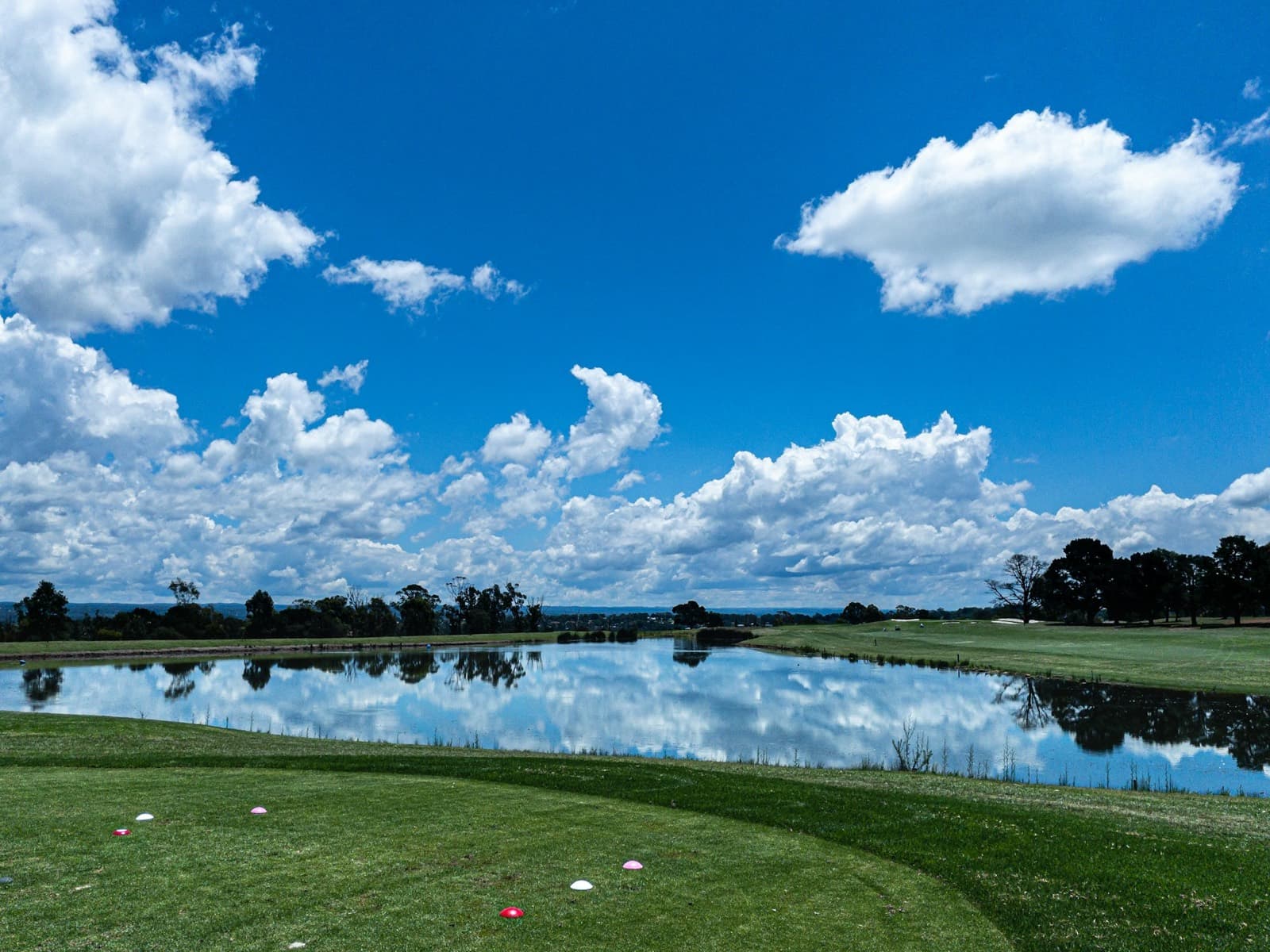 A tee box above a lake under a blue sky and white clouds