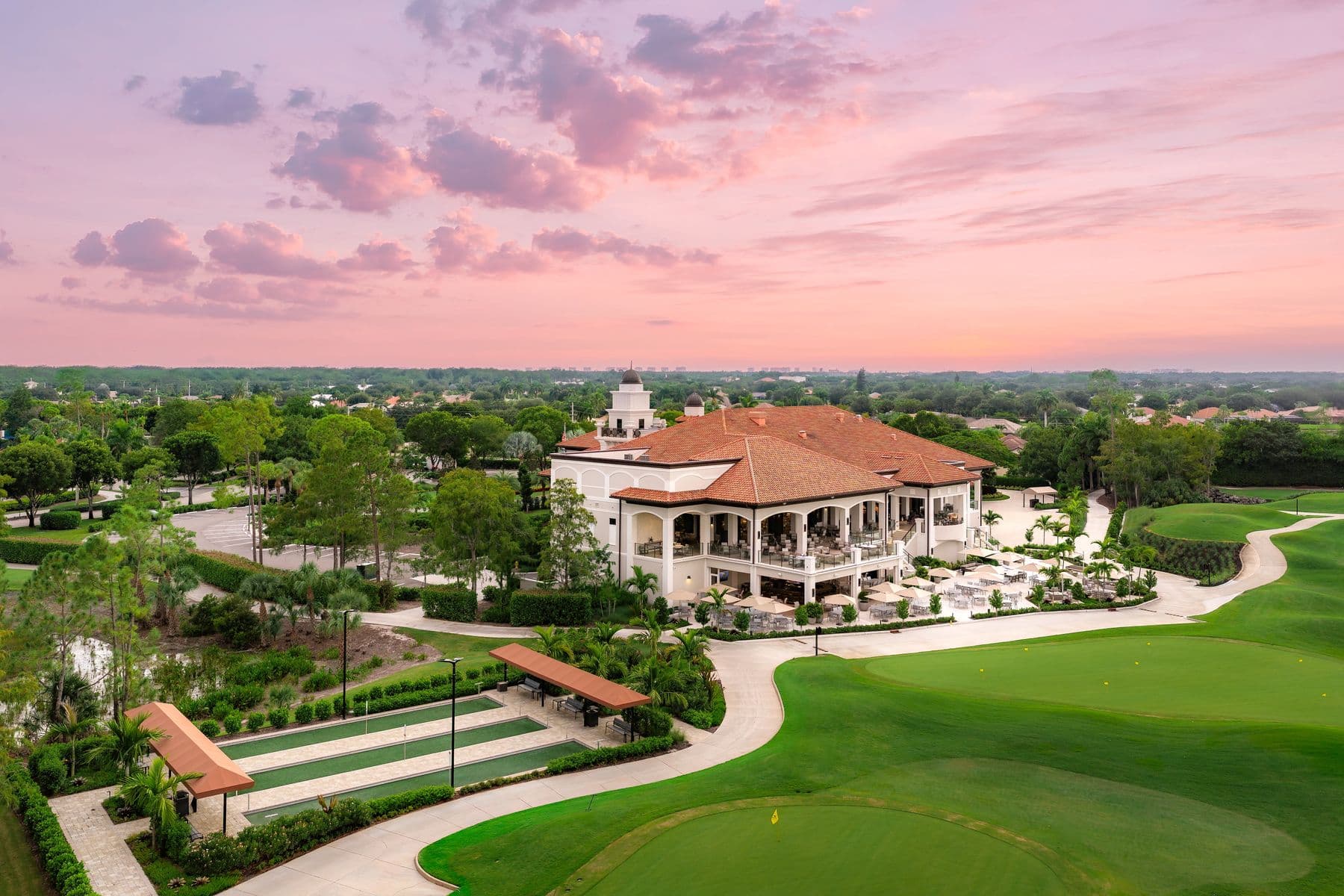The clubhouse at Olde Cypress from above at sunset, with the bocce courts and a green in front of it